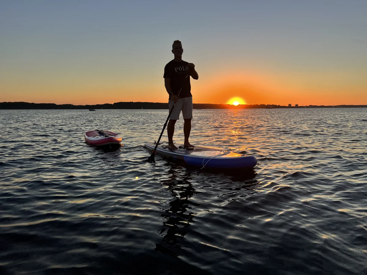 Stand-up-Paddling im orangefarbenen Sonnenuntergang.