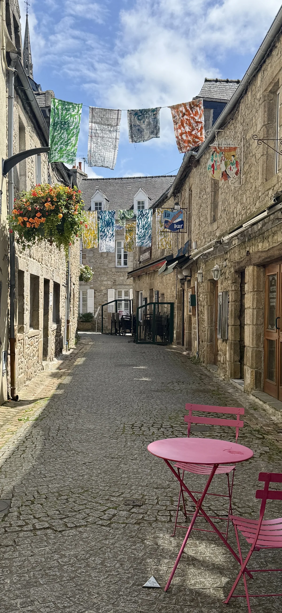 Sonnige Gasse mit bunten Wimpeln und pinken Stühlen.
