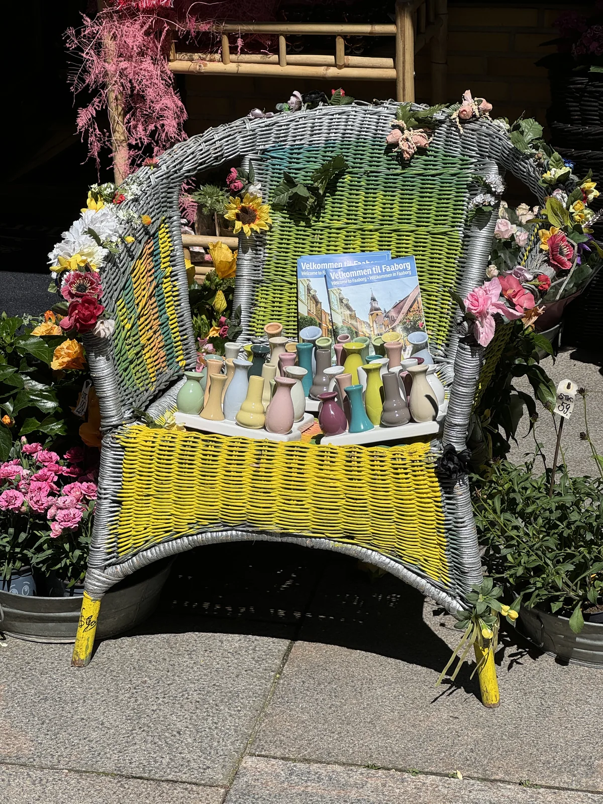 Kleine bunte Vasen auf einem mit Blumen geschmückten Korbstuhl.